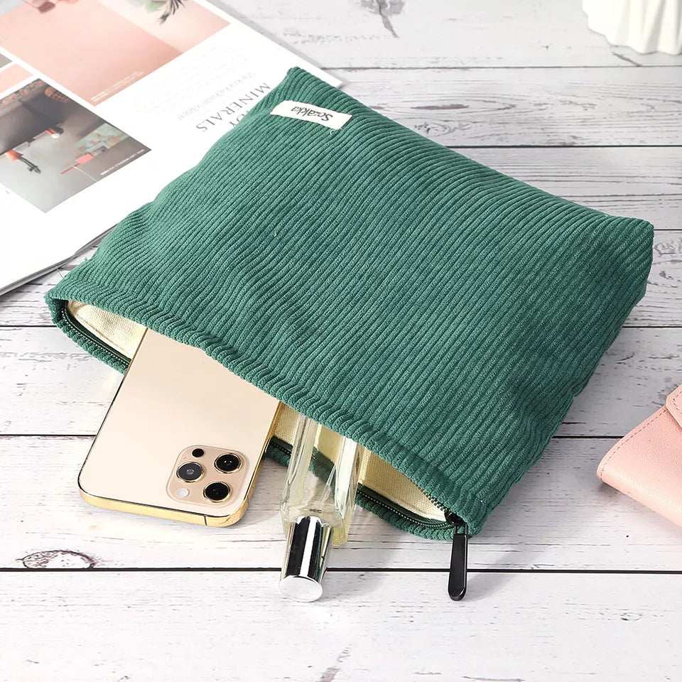 Astuccio verde in tessuto a coste con zip, contenente uno smartphone e un flacone di profumo. Accessorio moda pratico ed elegante per organizzare oggetti personali.