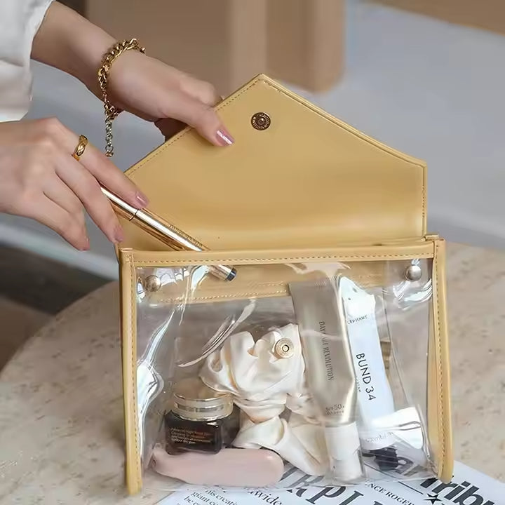 Borsa trasparente in PVC con dettagli in pelle gialla, contenente cosmetici e accessori. Ideale per viaggi, moda, organizzazione trucco.