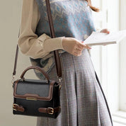 Borsa a tracolla in pelle nera e marrone, design elegante con fibbie dorate, indossata da donna in abbigliamento autunnale. Accessorio moda chic.