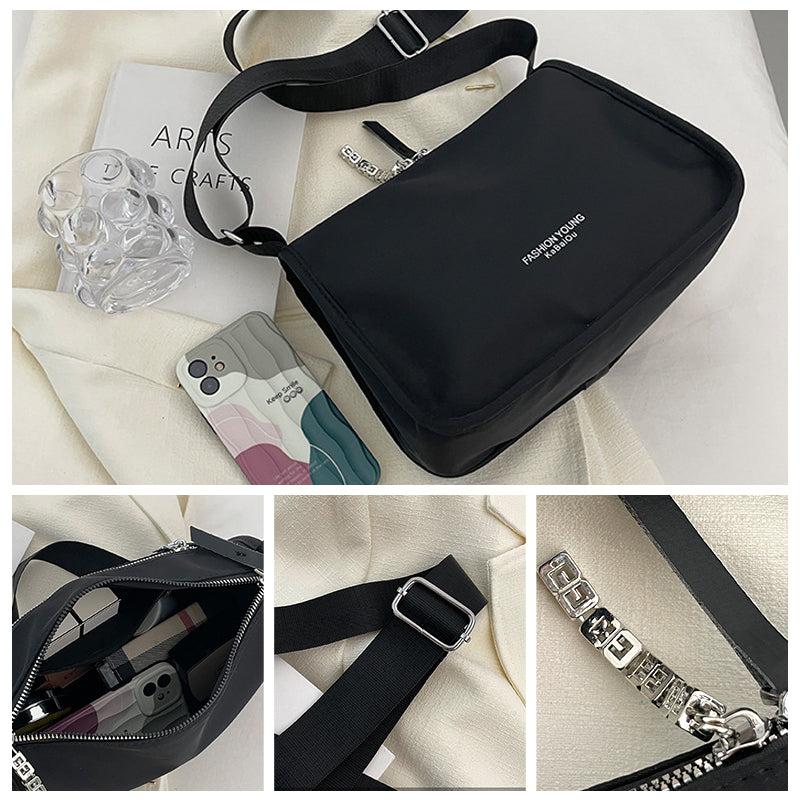 Borsa a tracolla nera in tessuto, con cerniera e dettagli metallici, accanto a un bicchiere trasparente e smartphone. Accessorio moda elegante e pratico.