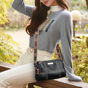 Donna con borsa a tracolla nera in pelle, design elegante con cuciture bianche, seduta su panchina in un parco autunnale. Moda femminile casual.