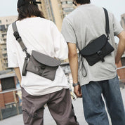 Due persone con marsupi a tracolla in città. Marsupio nero e grigio, stile casual urbano, moda streetwear, abbigliamento giovane e moderno.