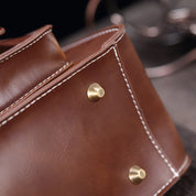Borsa in pelle marrone con cuciture bianche e piedini metallici dorati, design elegante e resistente, accessorio moda di alta qualità.