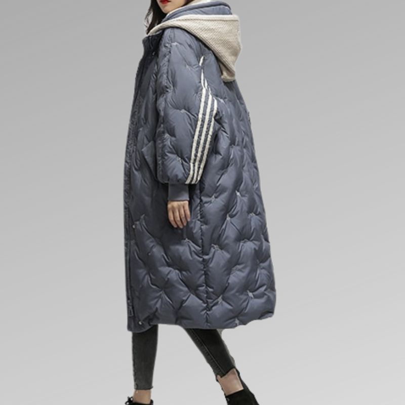 Giacca lunga trapuntata blu con cappuccio, dettagli a righe bianche sulle maniche, indossata da una donna. Moda invernale, abbigliamento caldo.