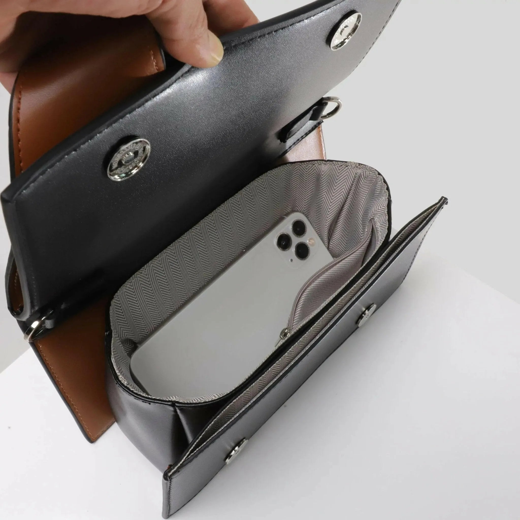 Borsa a tracolla in pelle nera aperta con interno foderato, contenente uno smartphone bianco. Design elegante e moderno, accessorio moda donna.