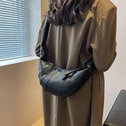Donna con cappotto marrone indossa borsa a tracolla in pelle nera, design moderno, elegante e versatile, perfetta per moda autunno inverno.