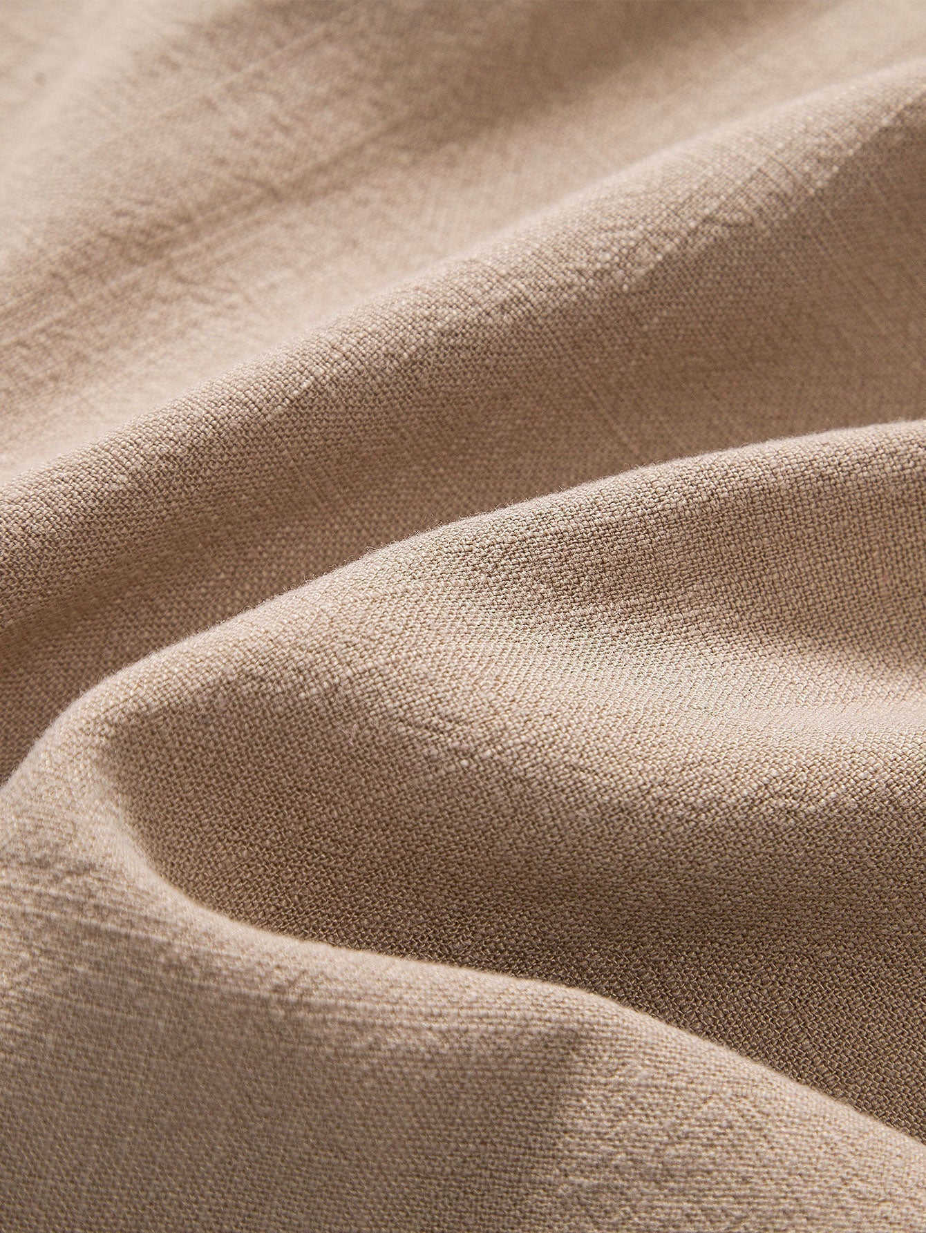 Tessuto di lino beige, trama naturale, texture morbida e ondulata, ideale per abbigliamento e arredamento, alta qualità e resistenza.