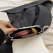 Borsa a tracolla bianca aperta su giacca nera, contenente portafoglio rosa, auricolari e smartphone. Accessori moda donna eleganti e pratici.