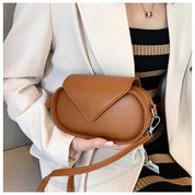 Borsa a tracolla in pelle marrone, design elegante e moderno, indossata da una donna in abito a righe. Accessorio moda femminile di tendenza.