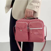 Borsa a tracolla rosa in nylon con tasche multiple e zip, manico superiore, indossata da una persona in abito chiaro. Accessorio moda elegante.