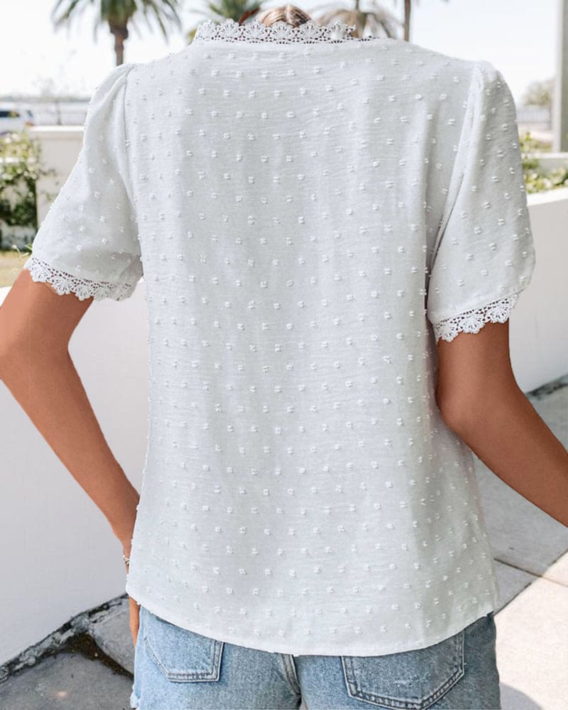 Maglietta bianca a pois con maniche corte e dettagli in pizzo, indossata da una persona all'aperto. Stile casual estivo, moda donna.