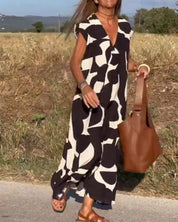 Abito lungo estivo donna con motivo astratto bianco e nero, borsa in pelle marrone, sandali marroni, sfondo campagna. Moda casual elegante.