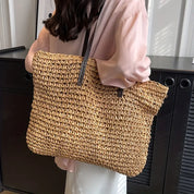Donna con borsa a tracolla in paglia intrecciata, stile casual, manici in pelle marrone, perfetta per l'estate e lo shopping.