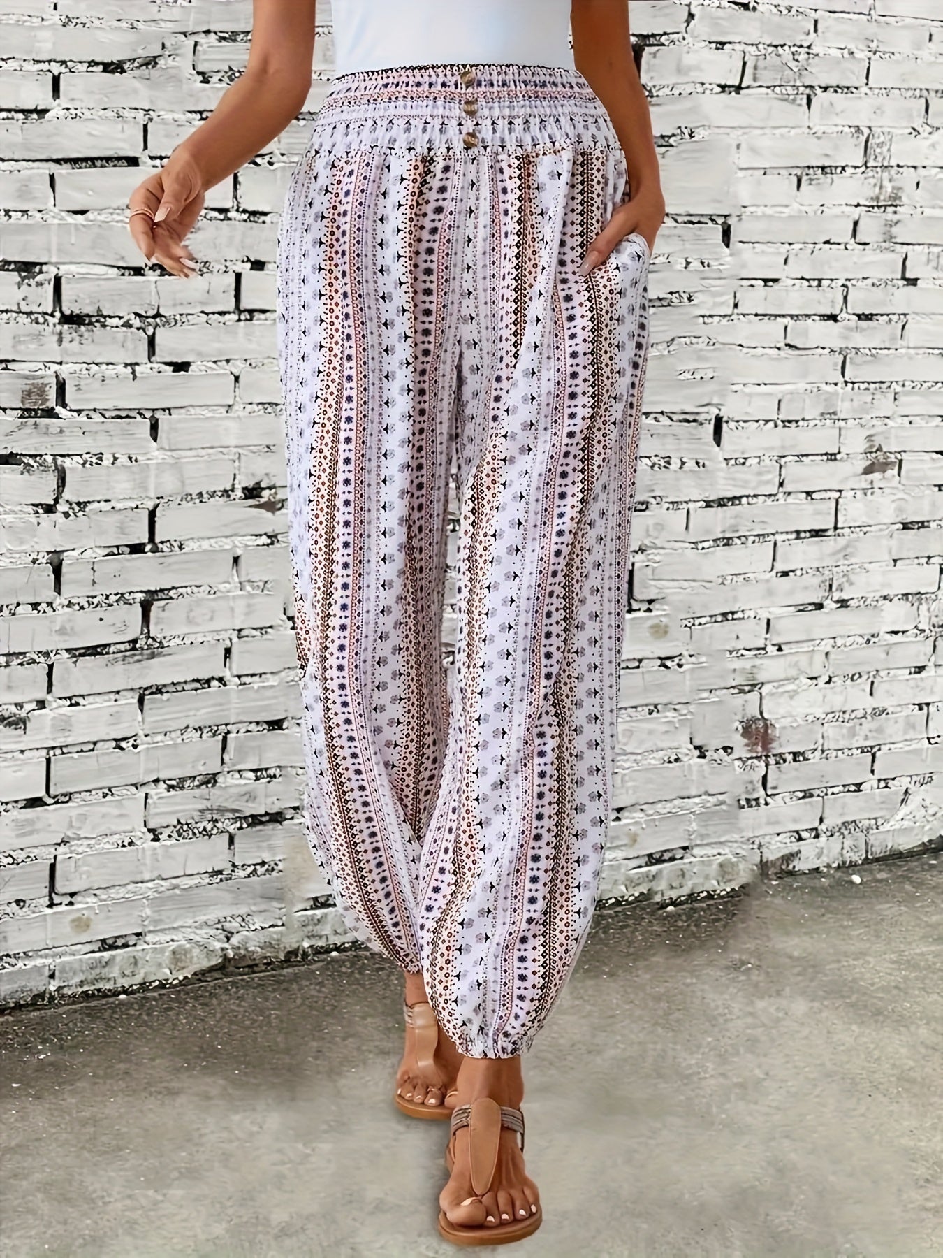Pantaloni estivi donna a palazzo, bianchi con motivo geometrico nero, elastico in vita, tasche laterali, indossati con sandali marroni.