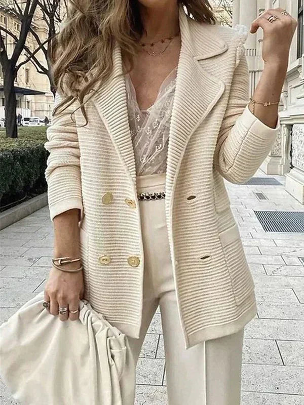 Donna con blazer beige a coste, top in pizzo e pantaloni coordinati, tiene una borsa morbida. Look elegante e chic per moda autunnale.