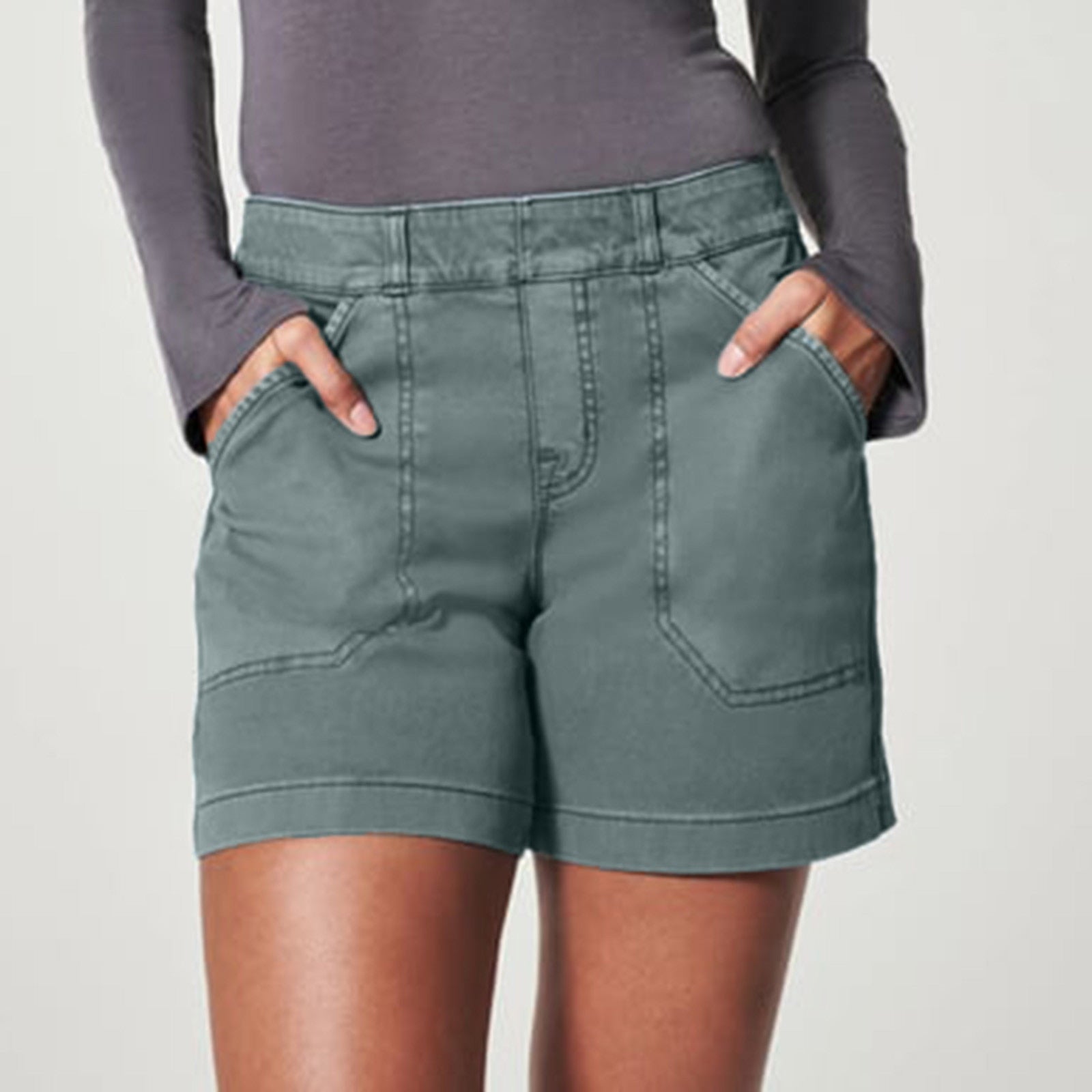 Donna in pantaloncini verdi, tasche frontali, maglia a maniche lunghe grigia. Moda casual, abbigliamento estivo, stile confortevole.