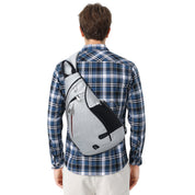 Uomo con zaino monospalla grigio, design moderno, indossa camicia a quadri blu. Accessorio moda casual, ideale per viaggi e uso quotidiano.
