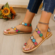 Sandali estivi da donna con cinturino, decorati con perline colorate, su pavimento in legno. Scarpe moda casual, ideali per look estivi.