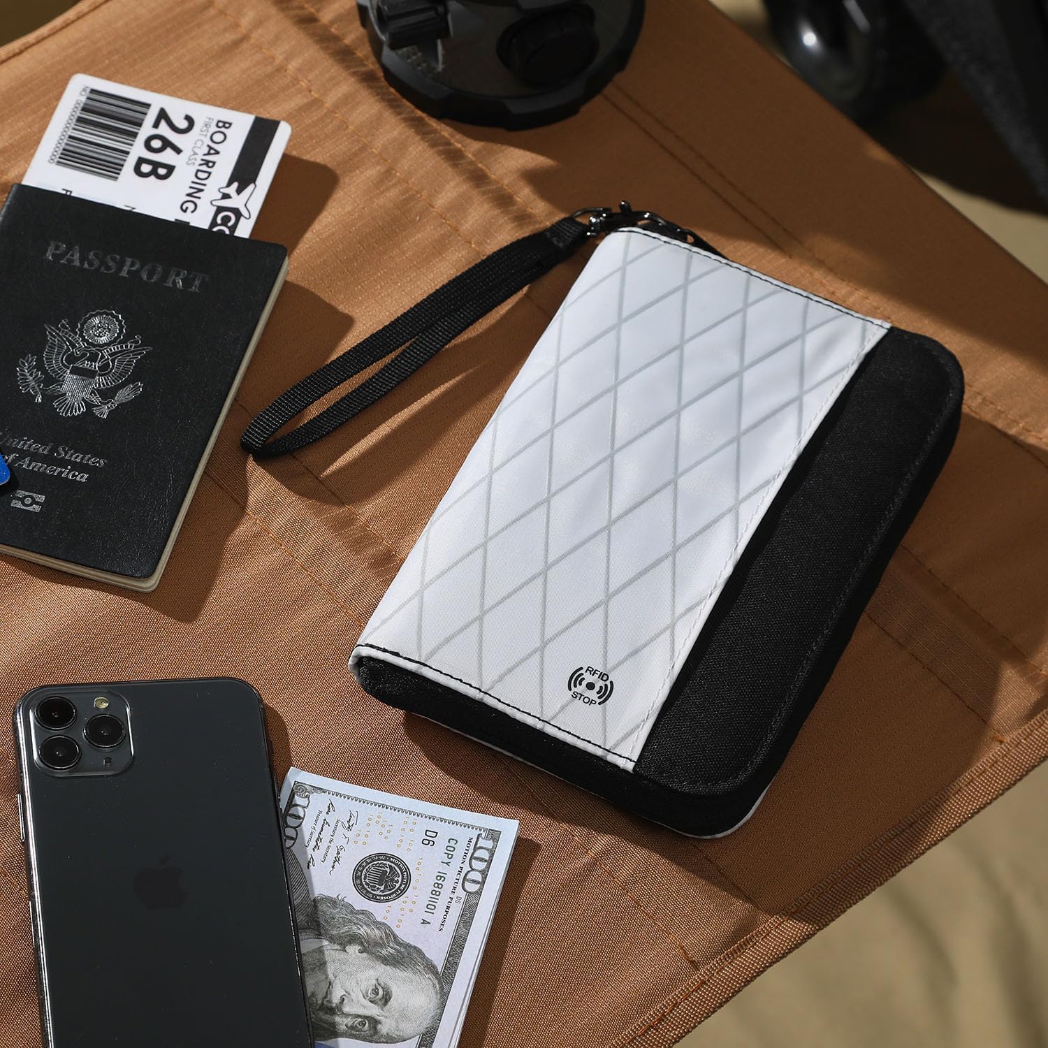 Portafoglio da viaggio bianco e nero con chiusura a zip, posizionato su un tavolo marrone, accanto a passaporto, smartphone e banconota da 100 dollari.