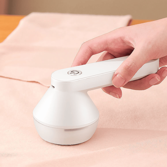 Rimuovi pelucchi elettrico bianco, portatile, in uso su tessuto rosa. Design ergonomico, ideale per abbigliamento e tessuti. Accessorio per la cura dei vestiti.