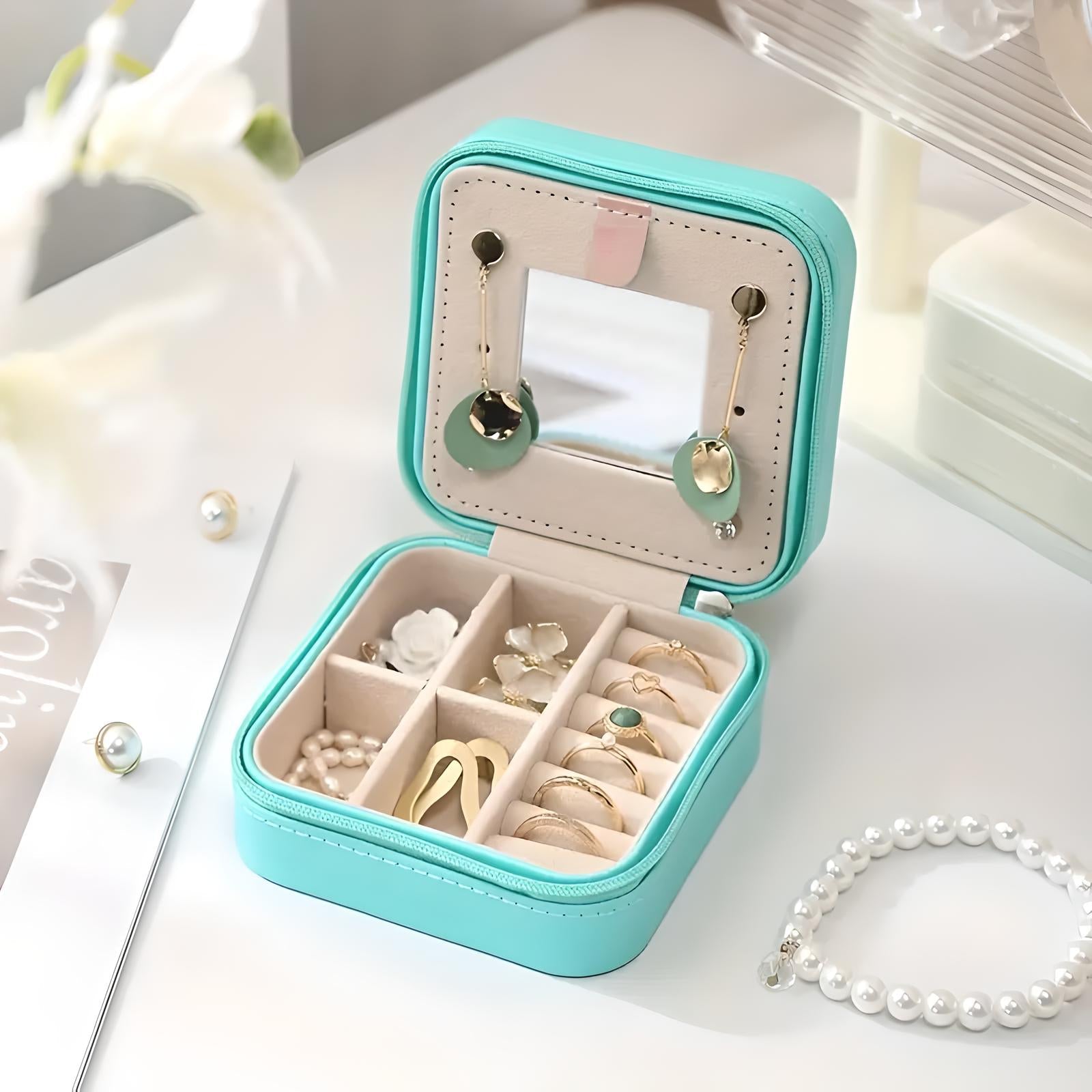 Astuccio portagioie turchese aperto con specchio, orecchini pendenti, anelli e perle. Organizzatore compatto per gioielli, ideale per viaggi.