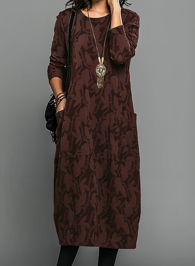 Abito lungo marrone con motivo floreale, maniche lunghe, tasche laterali, collana pendente. Elegante e casual, perfetto per l'autunno.