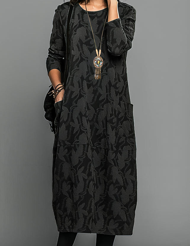 Abito lungo nero con motivo floreale, maniche lunghe, tasche laterali, collana pendente. Moda donna elegante, abbigliamento autunnale casual.