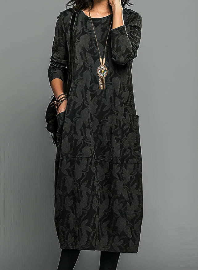 Abito lungo nero con motivo floreale, maniche lunghe, tasche laterali, collana pendente. Moda donna elegante, abbigliamento autunnale casual.