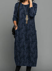 Abito lungo blu scuro con motivo floreale, maniche lunghe, tasche laterali e collana pendente. Stile casual elegante per donna.