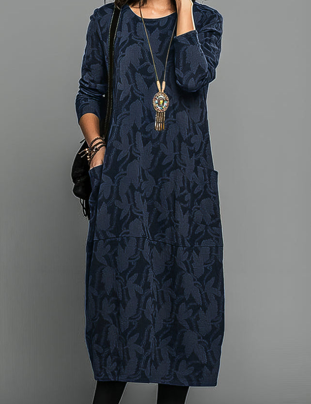 Abito lungo blu scuro con motivo floreale, maniche lunghe, tasche laterali e collana pendente. Stile casual elegante per donna.