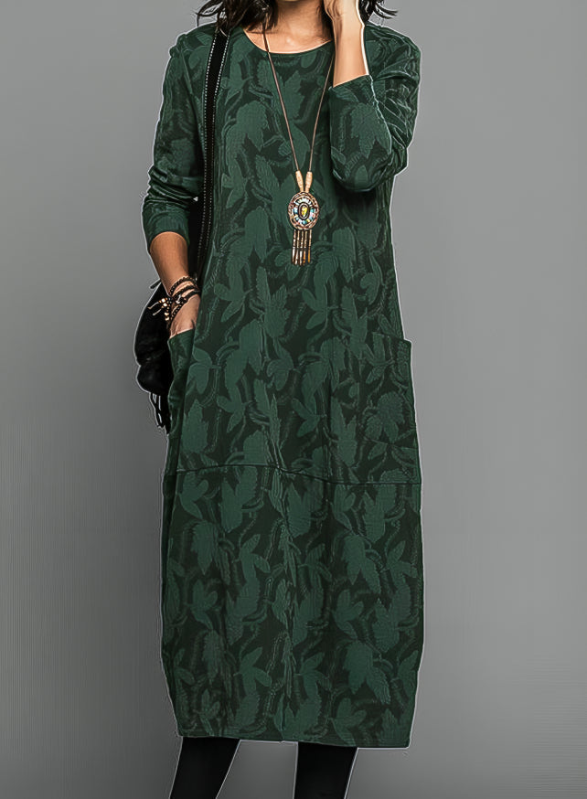 Abito lungo verde con motivo floreale, maniche lunghe, tasche frontali, collana pendente. Elegante e casual, perfetto per l'autunno.