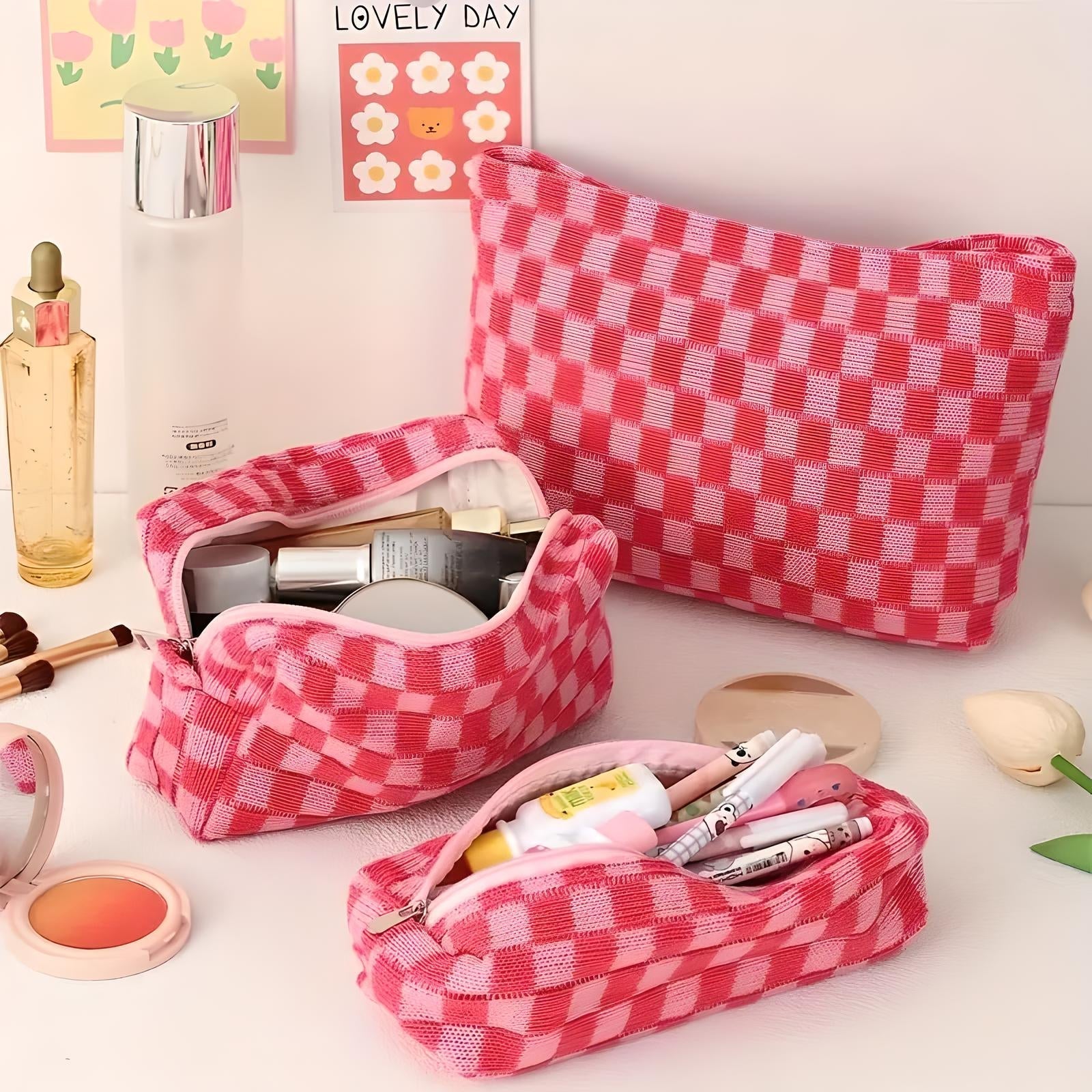 Set di tre astucci cosmetici a quadretti rosa, contenenti trucchi e accessori di bellezza. Ideale per organizzare prodotti cosmetici da viaggio.