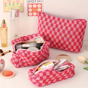 Set di tre astucci cosmetici a quadretti rosa, contenenti trucchi e accessori di bellezza. Ideale per organizzare prodotti cosmetici da viaggio.