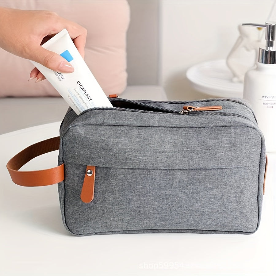 Borsa da toilette grigia con manico in pelle, tasca frontale e zip, contenente un tubetto di crema. Ideale per viaggi e organizzazione bagno.