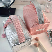 Due beauty case intrecciati, uno rosa e uno argento, su un tavolo con pennelli trucco. Eleganti e moderni, ideali per organizzare cosmetici.