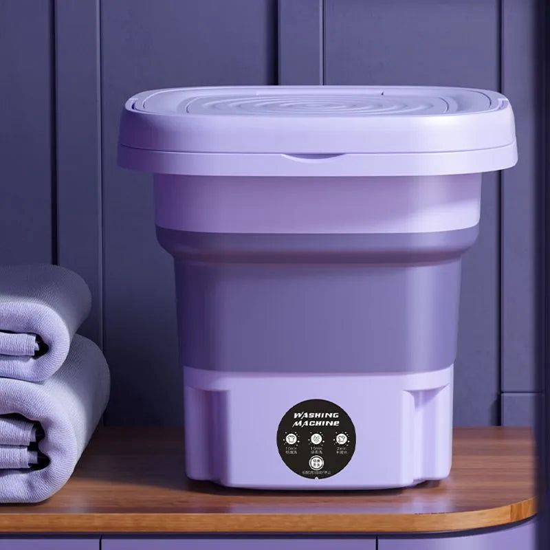 Lavatrice portatile pieghevole viola su mobile in legno, ideale per piccoli spazi. Design compatto, perfetta per viaggi e uso domestico.