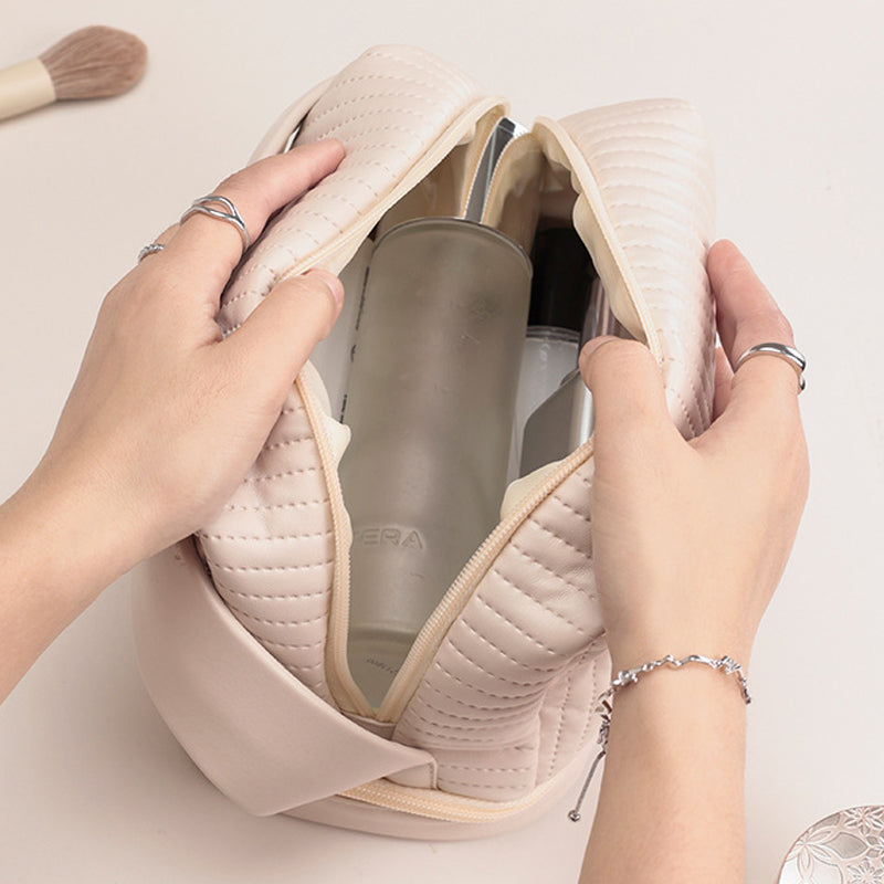 Borsa cosmetica beige trapuntata aperta, contenente flaconi di prodotti per la cura della pelle. Mani femminili con anelli e bracciale.