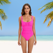 Donna in costume intero rosa su spiaggia tropicale, cielo azzurro e palme. Moda mare, abbigliamento estivo, vacanza al mare.