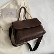 Borsa a tracolla in pelle marrone con texture coccodrillo su sfondo chiaro, elegante e versatile, perfetta per moda donna e accessori di lusso.
