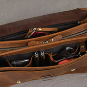 Borsa in pelle marrone aperta, con scomparti organizzati contenenti penne, chiavi e un passaporto. Design elegante e funzionale per viaggi d'affari.