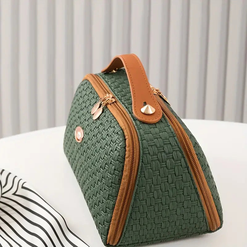 Borsa a mano verde intrecciata con manico marrone, chiusura a zip dorata, su tavolo bianco. Elegante accessorio moda donna.