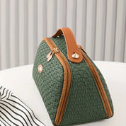 Borsa a mano verde intrecciata con manico marrone, chiusura a zip dorata, su tavolo bianco. Elegante accessorio moda donna.