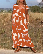 Donna con abito lungo estivo arancione e bianco a motivi astratti, sandali marroni, in un campo all'aperto. Moda femminile, abbigliamento estivo.