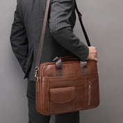 Uomo in abito grigio con borsa a tracolla in pelle marrone, elegante e professionale, ideale per lavoro e ufficio.