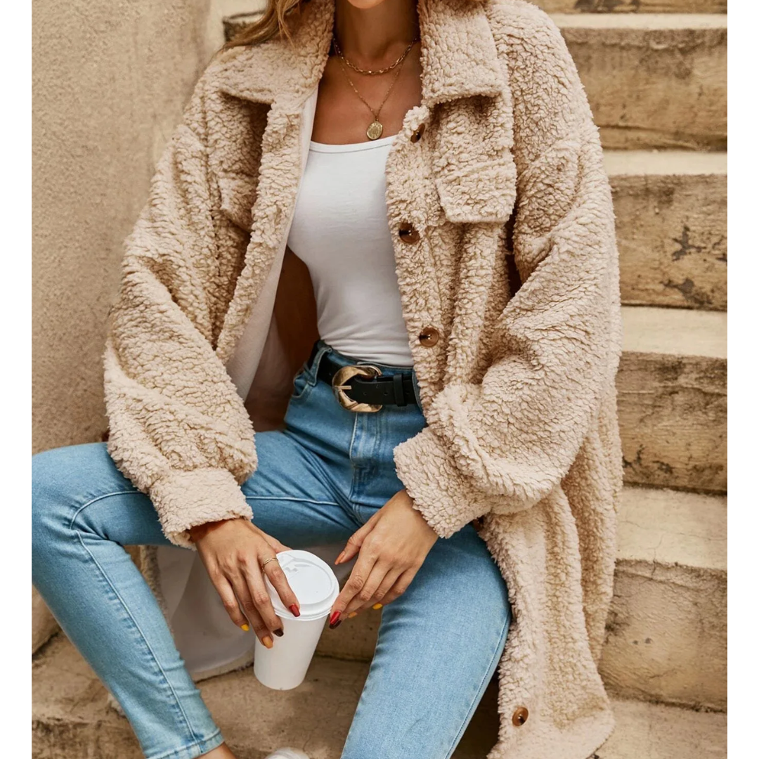 Donna con cappotto teddy beige, jeans attillati e cintura nera, tiene una tazza da caffè. Moda autunnale casual, abbigliamento caldo e confortevole.