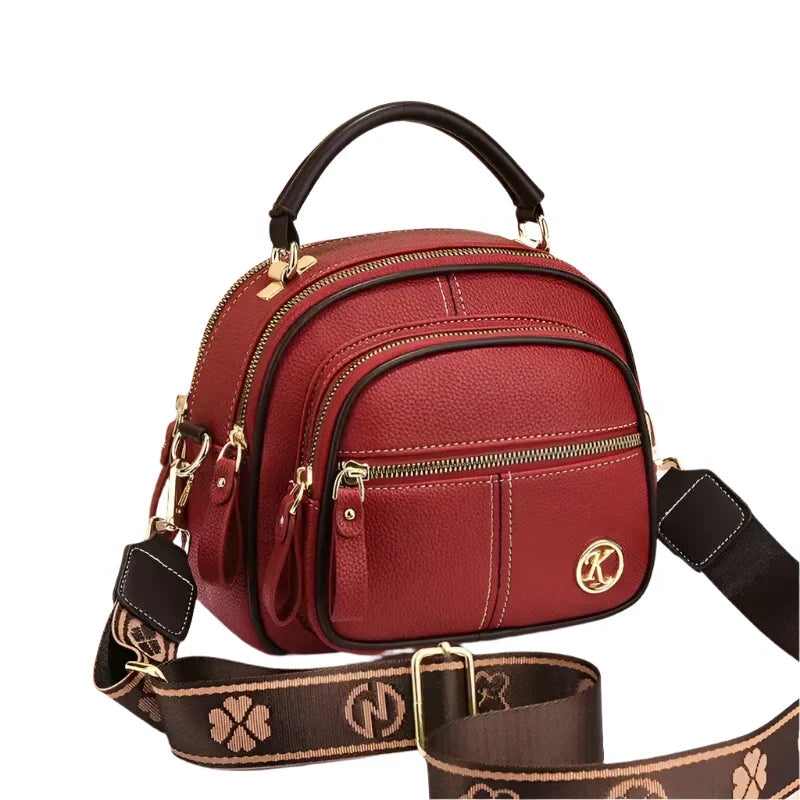 Borsa a tracolla in pelle rossa con manico superiore, cerniere dorate e logo decorativo. Design elegante, ideale per moda donna e accessori.