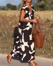 Donna con abito lungo bianco e nero astratto, borsa in pelle marrone, sandali marroni, cammina su strada di campagna. Moda estiva, stile casual.