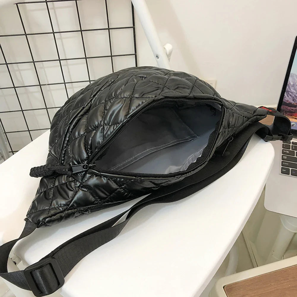 Borsa a tracolla nera trapuntata aperta su sedia bianca, design moderno, chiusura a zip, ideale per moda urbana e viaggi.