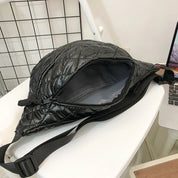 Borsa a tracolla nera trapuntata aperta su sedia bianca, design moderno, chiusura a zip, ideale per moda urbana e viaggi.