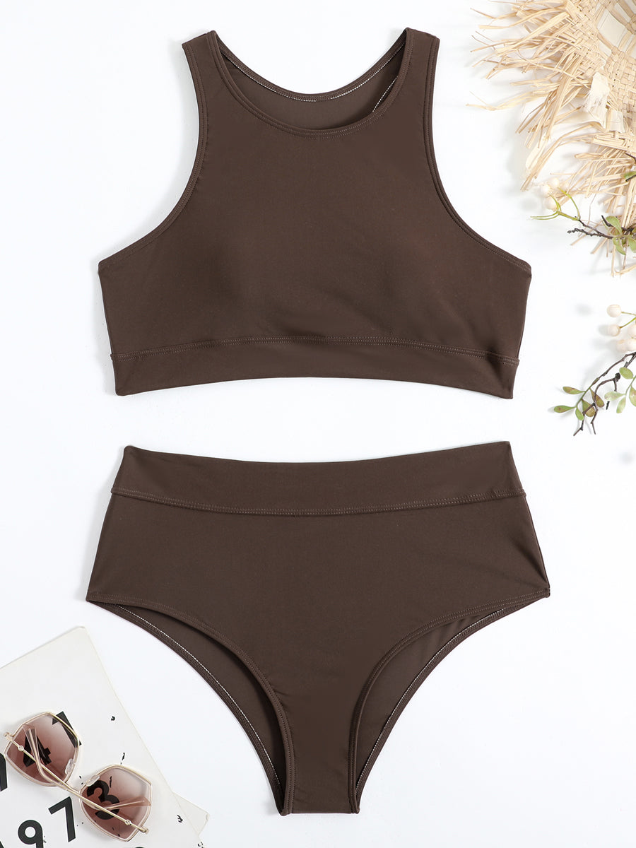 Costume da bagno donna marrone scuro a due pezzi, top sportivo e slip a vita alta, su sfondo bianco con occhiali da sole e decorazioni naturali.